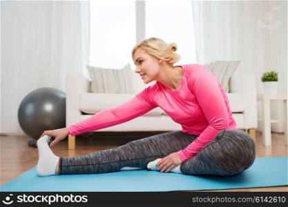 fitness, sport, people and healthy lifestyle concept - happy plus size woman stretching leg on mat at home