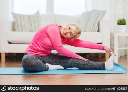 fitness, sport, people and healthy lifestyle concept - happy plus size woman stretching leg on mat at home
