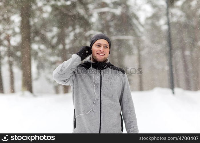 fitness, sport, people and healthy lifestyle concept - happy smiling young man with earphones listening to music in winter forest