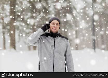 fitness, sport, people and healthy lifestyle concept - happy smiling young man with earphones listening to music in winter forest. happy sports man with earphones in winter forest