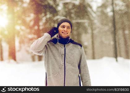 fitness, sport, people and healthy lifestyle concept - happy smiling young man with earphones listening to music in winter forest. happy sports man with earphones in winter forest