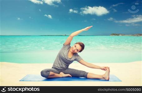 fitness, sport, people and healthy lifestyle concept - happy woman making yoga and stretching on mat over sea and sky background. happy woman making yoga and stretching on beach