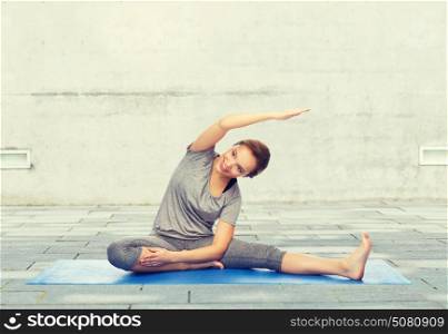 fitness, sport, people and healthy lifestyle concept - happy woman making yoga and stretching on mat over urban street background. happy woman making yoga and stretching on mat