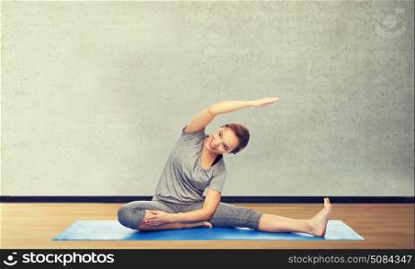 fitness, sport, people and healthy lifestyle concept - happy woman making yoga and stretching on mat over gym room background. happy woman making yoga and stretching on mat. happy woman making yoga and stretching on mat