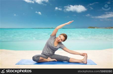 fitness, sport, people and healthy lifestyle concept - happy woman making yoga and stretching on mat over sea and sky background