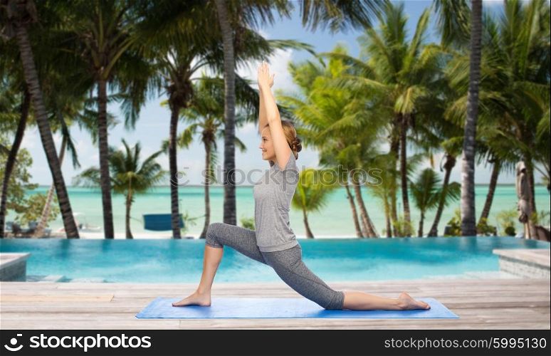 fitness, sport, people and healthy lifestyle concept - happy woman making yoga in low lunge pose on mat over swimming pool and palm trees at hotel resort background