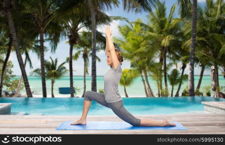 fitness, sport, people and healthy lifestyle concept - happy woman making yoga in low lunge pose on mat over swimming pool and palm trees at hotel resort background