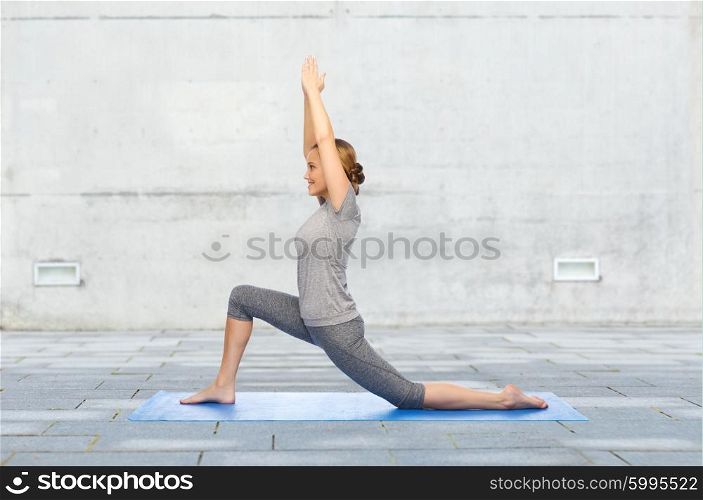fitness, sport, people and healthy lifestyle concept - happy woman making yoga in low lunge pose on mat over urban street background