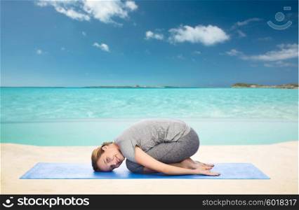 fitness, sport, people and healthy lifestyle concept - happy woman making yoga in child pose on mat over sea and sky background