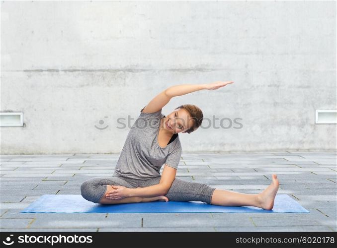 fitness, sport, people and healthy lifestyle concept - happy woman making yoga and stretching on mat over urban street background