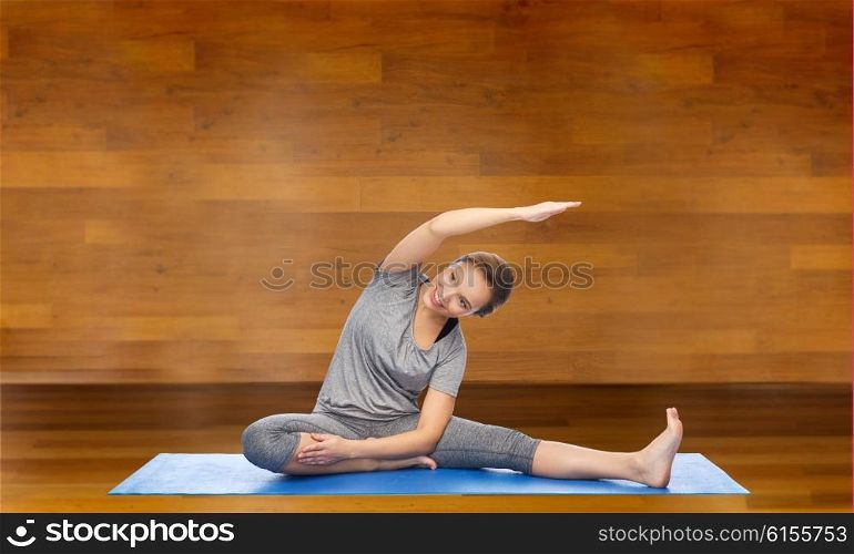 fitness, sport, people and healthy lifestyle concept - happy woman making yoga and stretching on mat over wooden room background
