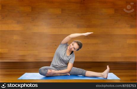 fitness, sport, people and healthy lifestyle concept - happy woman making yoga and stretching on mat over wooden room background