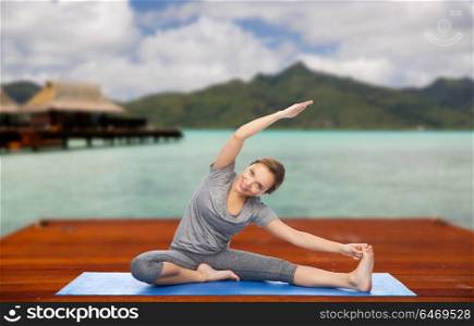 fitness, sport, people and healthy lifestyle concept - happy woman making yoga and stretching on wooden pier over island beach and bungalow background. happy woman making yoga and stretching outdoors