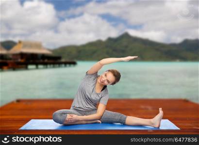 fitness, sport, people and healthy lifestyle concept - happy woman making yoga and stretching on wooden pier over island beach and bungalow background. happy woman making yoga and stretching outdoors. happy woman making yoga and stretching outdoors