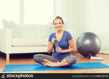fitness, sport, people and healthy lifestyle concept - happy woman with bottle of water after exercising on mat at home. happy woman with water bottle exercising at home