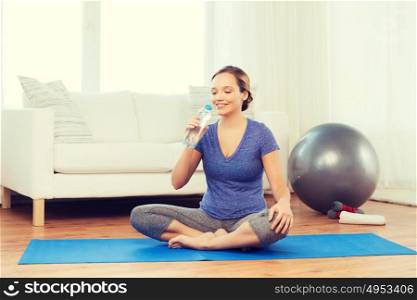 fitness, sport, people and healthy lifestyle concept - happy woman with bottle of water after exercising on mat at home. happy woman with water bottle exercising at home