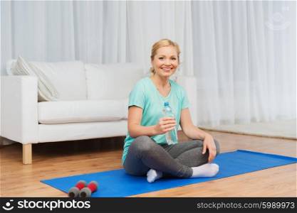 fitness, sport, people and healthy lifestyle concept - happy woman with bottle of water after exercising on mat at home