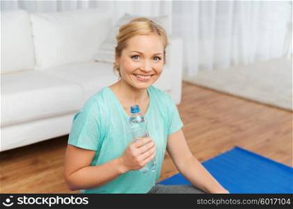 fitness, sport, people and healthy lifestyle concept - happy woman with bottle of water after exercising on mat at home