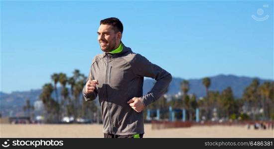 fitness, sport, people and healthy lifestyle concept - happy young man running over venice beach background in california. happy young man running over venice beach. happy young man running over venice beach