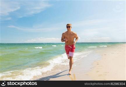 fitness, sport, people and healthy lifestyle concept - happy young man running along summer beach. happy man running along summer beach