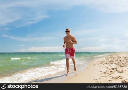 fitness, sport, people and healthy lifestyle concept - happy young man with headphones running along summer beach. happy man with headphones running along beach