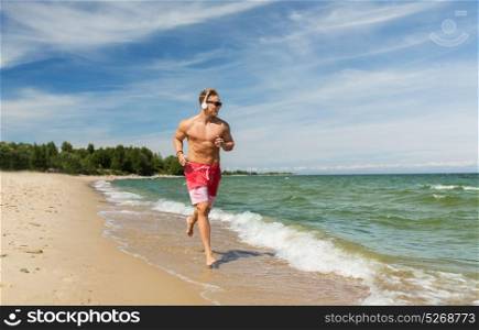 fitness, sport, people and healthy lifestyle concept - happy young man with headphones running along summer beach. happy man with headphones running along beach