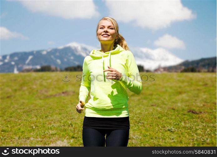 fitness, sport, people and healthy lifestyle concept - happy young smiling woman jogging or running over mountains, green field and blue sky background