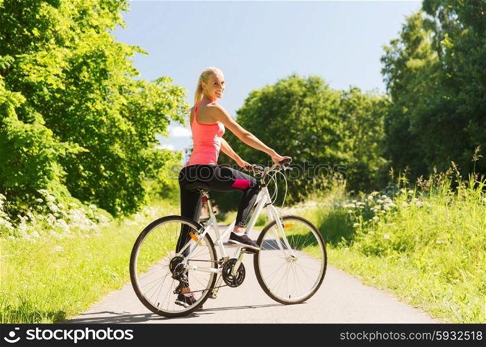 fitness, sport, people and healthy lifestyle concept - happy young woman riding bicycle outdoors