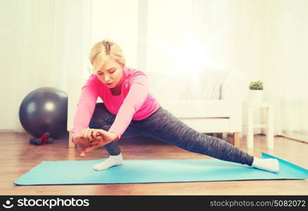 fitness, sport, people and healthy lifestyle concept - plus size woman stretching leg on mat at home. woman stretching leg on mat at home