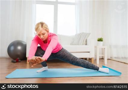 fitness, sport, people and healthy lifestyle concept - plus size woman stretching leg on mat at home