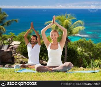 fitness, sport, people and healthy lifestyle concept - smiling couple making yoga in lotus posture sitting on mats outdoors over ocean background. smiling couple making yoga exercises outdoors