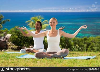 fitness, sport, people and healthy lifestyle concept - smiling couple making yoga in lotus posture sitting on mats outdoors over ocean background. smiling couple making yoga exercises outdoors