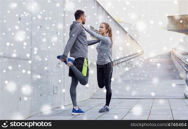 fitness, sport, people and healthy lifestyle concept - smiling couple of sportsmen stretching leg outdoors over snow