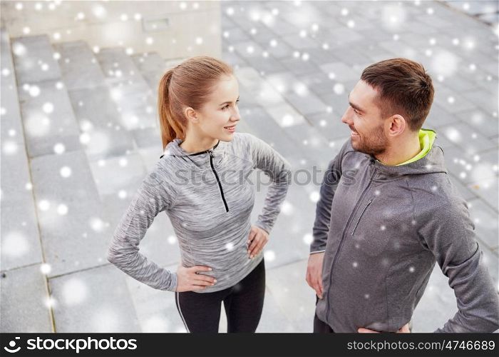 fitness, sport, people and healthy lifestyle concept - smiling couple of sportsmen outdoors on city street over snow