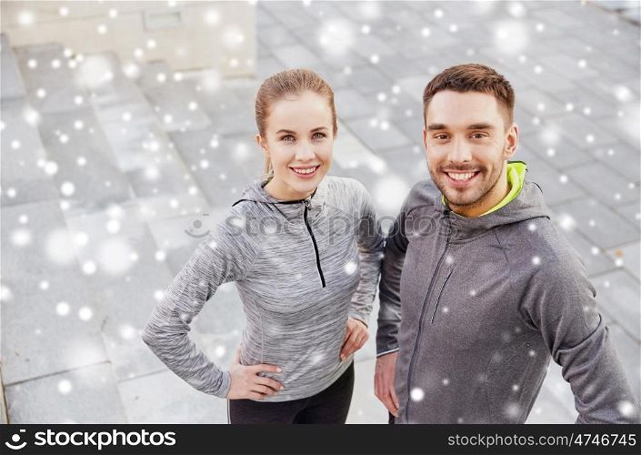 fitness, sport, people and healthy lifestyle concept - smiling couple of sportsmen outdoors on city street over snow