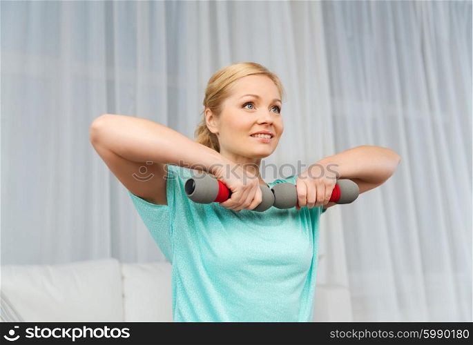 fitness, sport, people and healthy lifestyle concept - smiling woman exercising with dumbbells on mat at home