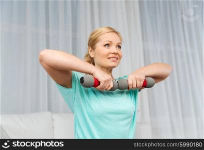 fitness, sport, people and healthy lifestyle concept - smiling woman exercising with dumbbells on mat at home