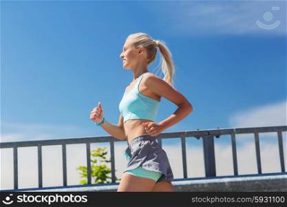 fitness, sport, people and healthy lifestyle concept - smiling young woman with heart rate watch running outdoors