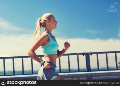 fitness, sport, people and healthy lifestyle concept - smiling young woman with heart rate watch running outdoors
