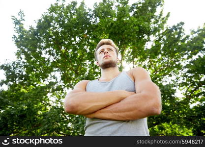 fitness, sport, people and healthy lifestyle concept - sporty young man with crossed arms at summer park