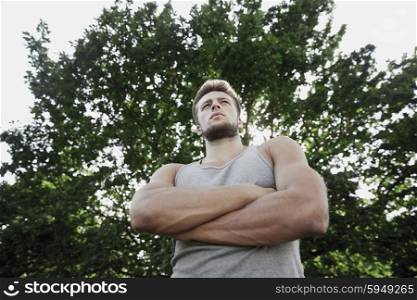 fitness, sport, people and healthy lifestyle concept - sporty young man with crossed arms at summer park