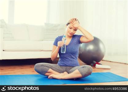 fitness, sport, people and healthy lifestyle concept - tired woman with bottle of water after exercising on mat at home. tired woman drinking water after workout at home