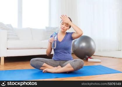 fitness, sport, people and healthy lifestyle concept - tired woman with bottle of water after exercising on mat at home