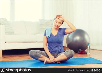 fitness, sport, people and healthy lifestyle concept - tired woman with towel after exercising on mat at home. tired woman with towel after workout at home