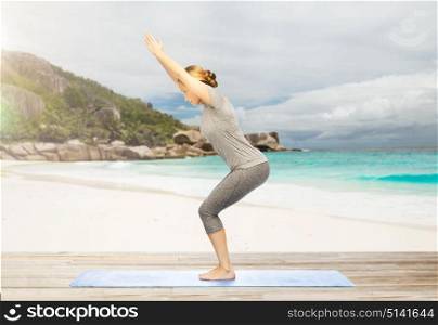 fitness, sport, people and healthy lifestyle concept - woman doing yoga chair pose on mat over exotic tropical beach background. woman doing yoga chair pose on beach