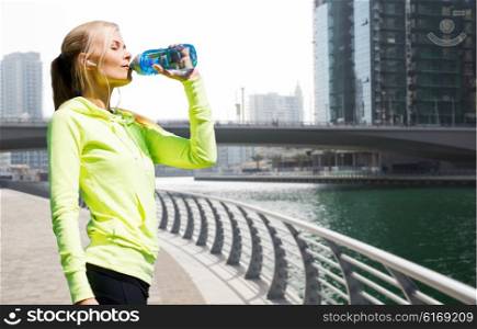 fitness, sport, people and healthy lifestyle concept - woman drinking water after doing sports over dubai city street or waterfront and bridge background