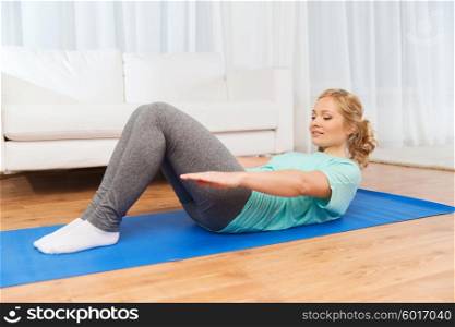 fitness, sport, people and healthy lifestyle concept - woman exercising on mat and doing sit-ups at home