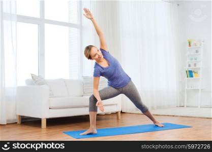 fitness, sport, people and healthy lifestyle concept - woman making yoga bikram triangle pose on mat