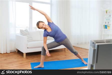 fitness, sport, people and healthy lifestyle concept - woman making yoga bikram triangle pose on mat