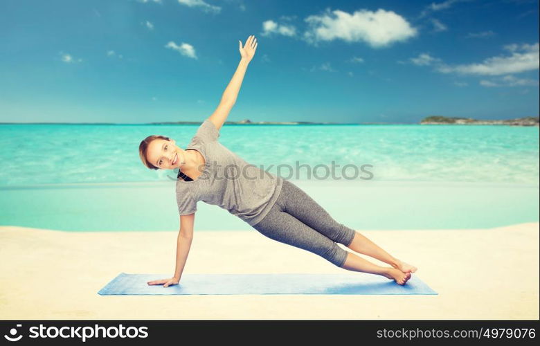 fitness, sport, people and healthy lifestyle concept - woman making yoga in side plank pose on mat over sea and sky background. woman making yoga in side plank pose on beach